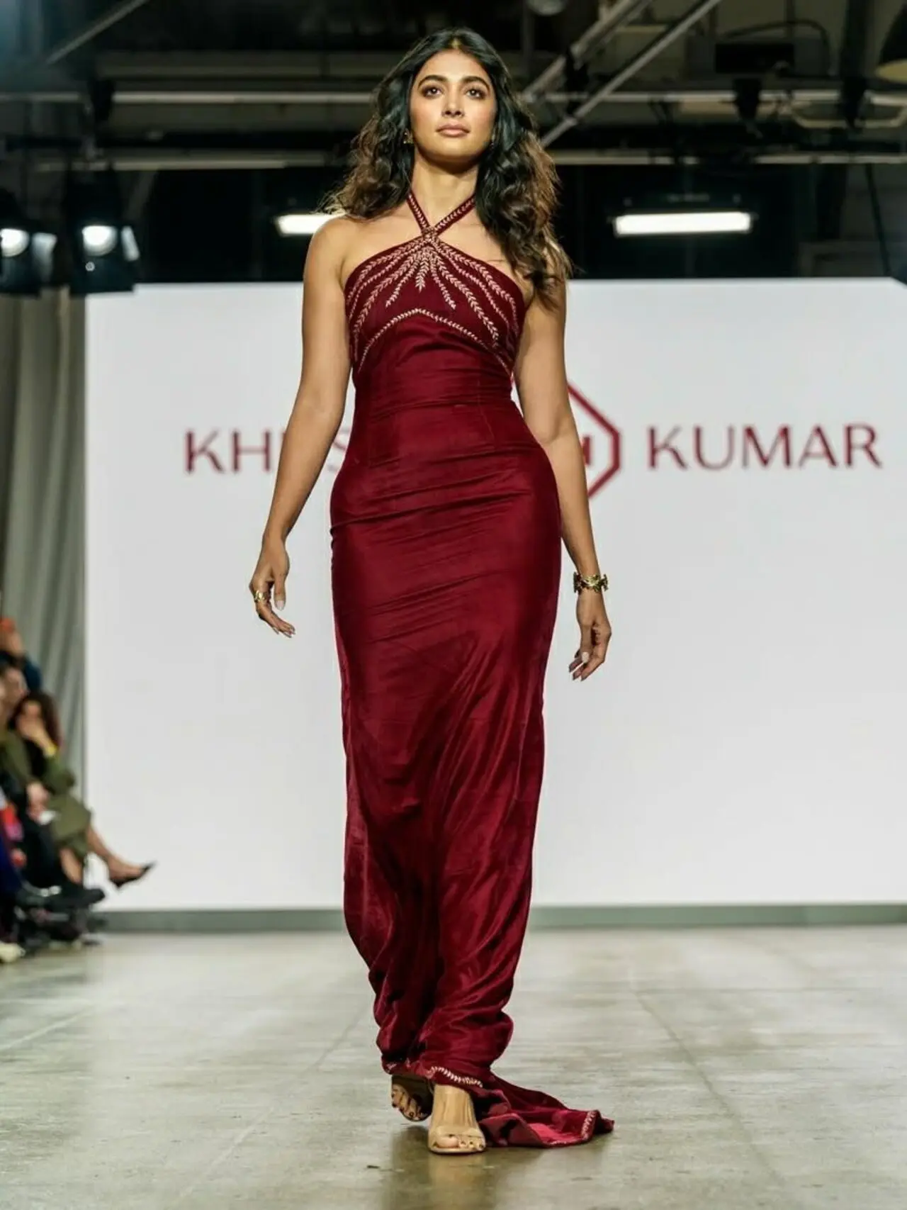 <p>Pooja Hegde hit the runway in a rich maroon halter-neck gown that skimmed her frame and trailed slightly behind her. The gold embroidery across the bodice caught the light in photos.</p>